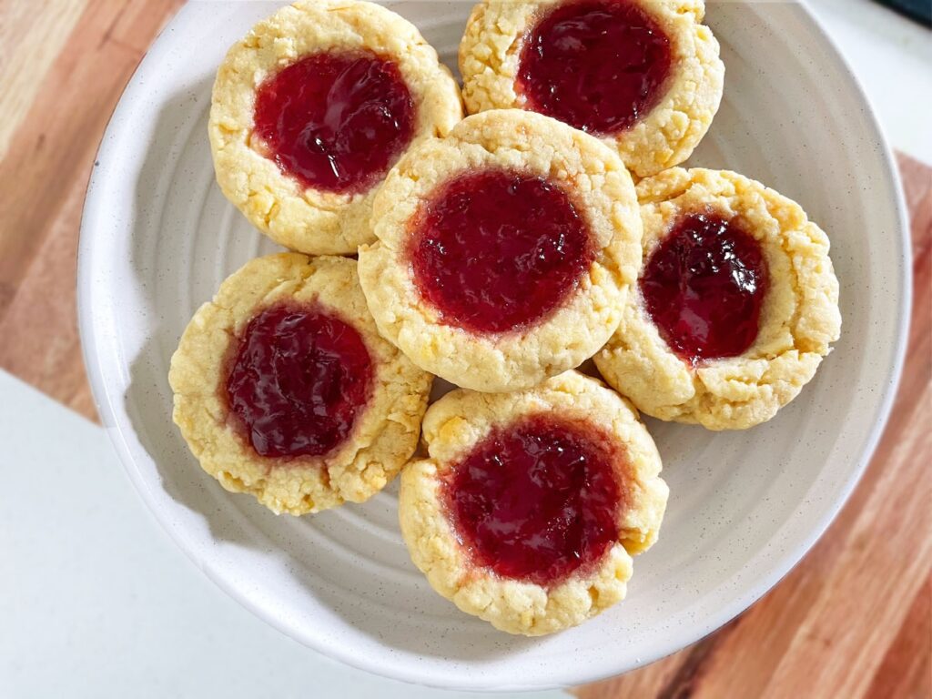 Freshly baked jam-filled scone-style cookies arranged on a white plate, showcasing their buttery, crumbly texture with vibrant jam centers