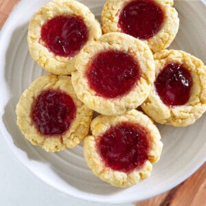 Freshly baked jam-filled scone-style cookies arranged on a white plate, showcasing their buttery, crumbly texture with vibrant jam centers